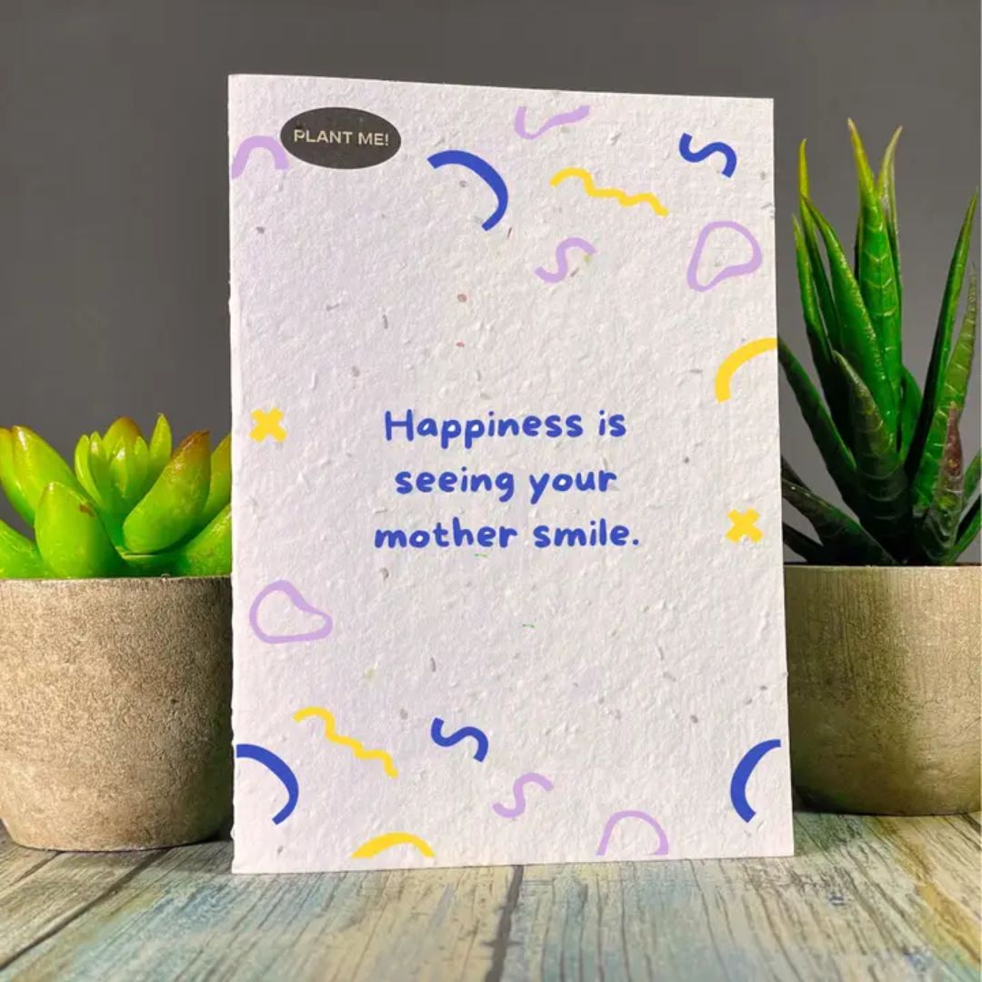 Seed paper greeting card with Happiness is seeing your mother smile in blue text, surrounded by blue, purple, and yellow streamers. Wordkind.