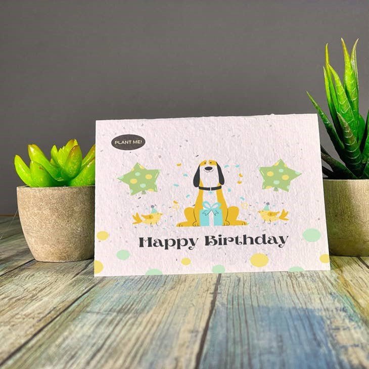 Seed paper birthday card featuring a dog in front of a gift, surrounded by chicks in party hats and star-shaped balloons. Wordkind.